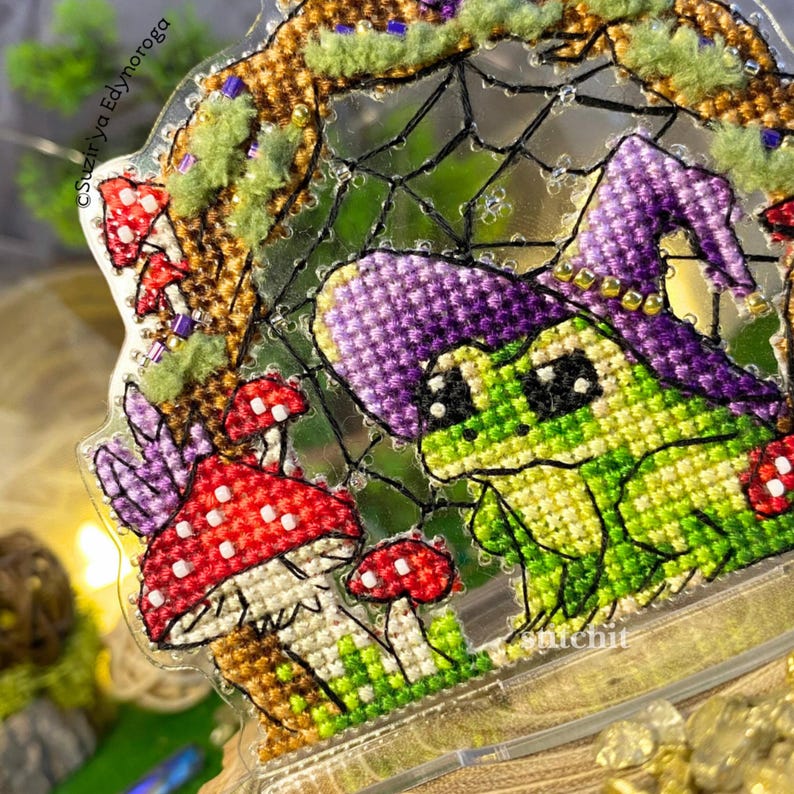 Halloween Frog Cross Stitch Kit — close-up detail of beaded frog in purple hat with mushrooms and mossy texture thread on clear plastic