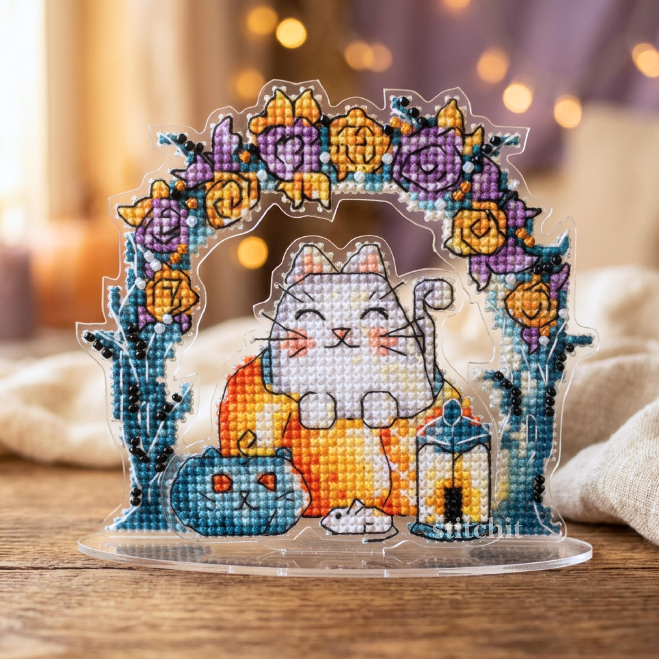 Cat Pumpkin Cross Stitch Kit — finished stitched cat with pumpkin and lantern under floral arch on clear plastic stand, cozy home decor display