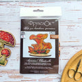Chanterelle Cross Stitch Kit on Wood — kit packaging with chart beside two finished embroidered mushrooms and scissors on a white surface.